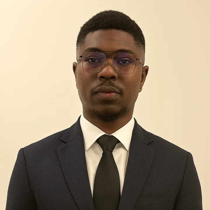 Joshua Odubu in a dark suit and tie, wearing glasses